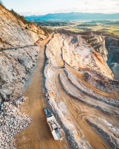 Aerial view of open pit quarry with heavy machinery working on the grounds. Excavators and trucks driving on the grounds. Sunny day in the countryside.